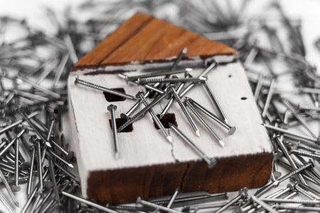 Wooden model of a residential building in a pile of metal nails. House construction and renovation concept. DIY ideasの写真素材