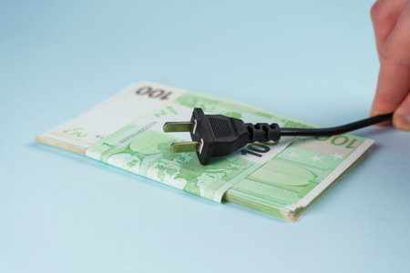 Power plug in hand on euro money background. Expensive electricity supply conceptの写真素材
