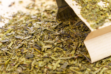 Scattered dried green sencha tea leaves with paper pack closeup. Healthy natural drinkの写真素材