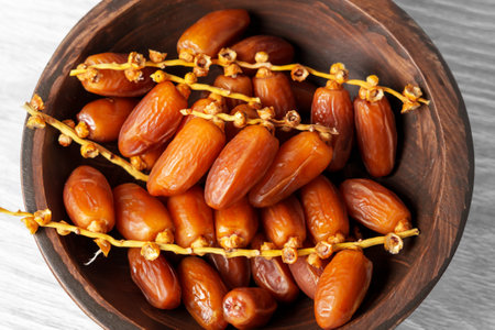 Sweet dried dates on a branch in wooden kitchen bowl. Oriental treats. Healthy nutritious snack. Top...