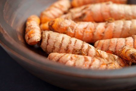 Organic turmeric roots in rustic wooden bowl. Many whole raw curcuma rhizomes. Indian natural...