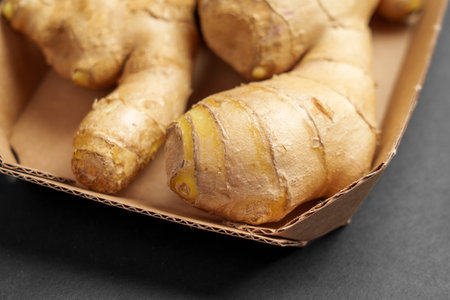 Whole raw ginger root or rhizome in paper packaging on a black background close up. Fresh herbal...