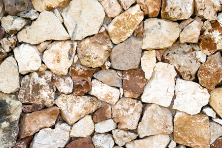 Exterior antique building wall from irregularly shaped stones in various shades of brown, beige and...