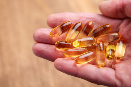 Translucent Omega-3 capsules in hand with dry wrinkled skin on a natural wooden background. Healthy supplement. Close upの写真素材