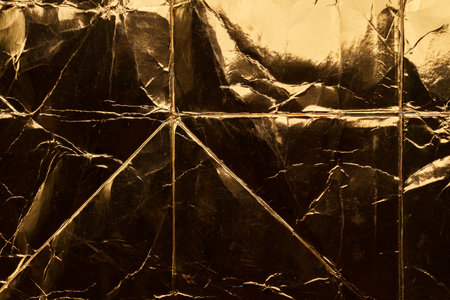 Old worn layered folded surface of wrinkled dusty gold foil sheet as crumpled luxury wrap and abstract backgroundの写真素材