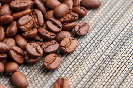 Roasted Arabica coffee beans scattered on a textured woven mat. Brown fragrant grains with natural...