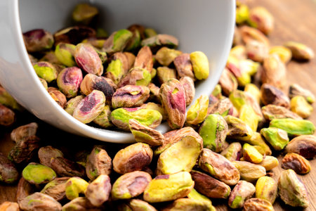 Peeled pistachio kernels in white cup are placed in pile of natural nutritious nuts. Macro shotの写真素材