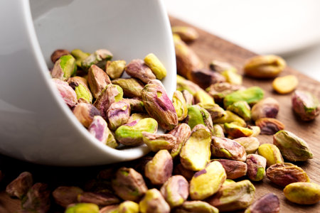 White ceramic cup in pile of peeled roasted pistachio kernels scattered on wooden table close-upの写真素材
