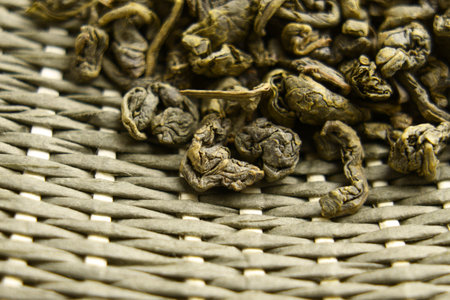 Dried leaves of Chinese traditional green tea on textured wicker mat. Macro shot.