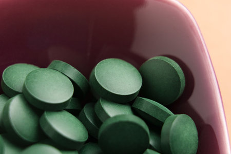 Green spirulina pills in red ceramic plate. Nutrition detox supplement. Macro shot.の写真素材