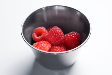 Fresh raspberries in round metal container on white tableの写真素材