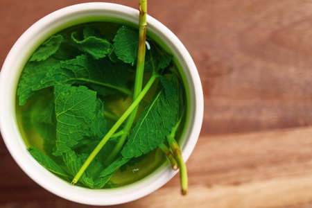 Fresh mint in mug of hot water on wooden table. Healing soothing herbal tea brewingの写真素材