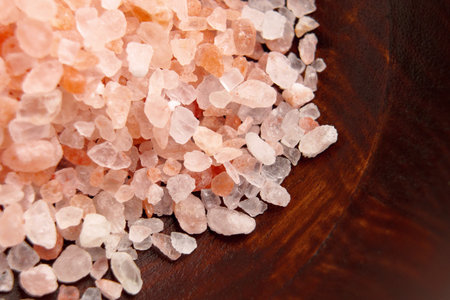 A pile of coarse Himalayan salt on a brown wooden surface. Macro shot.