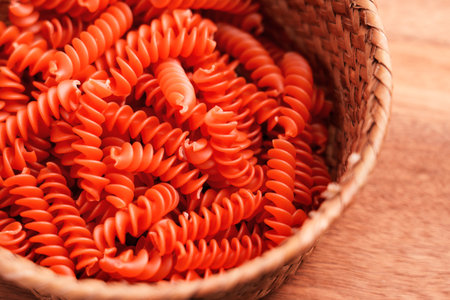 Red uncooked fusilli pasta in rustic eco friendly wicker bowl on wooden tableの写真素材