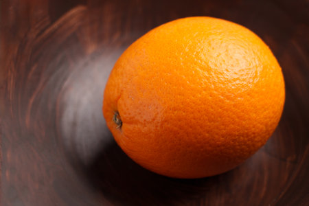 Single ripe orange on dark wooden bowl surface with natural citrus texture. Minimal food still life conceptの写真素材
