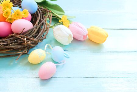 Colorful Easter eggs in nest with flowers on blue wooden background.