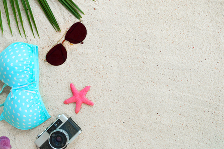Beach background.  Top view of beach sand with coconut leaves, sunglasses, bikini, starfish, shell and retro camera.  Summer background concept.の写真素材