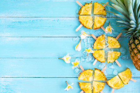 Pineapple popsicle sticks with ice on wood plank blue color. summer fruit concept, top viewの写真素材