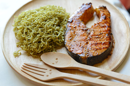 Grilled salmon and green noodle with smiley wooden spoon and fork. Concept about happiness and relationship.の写真素材