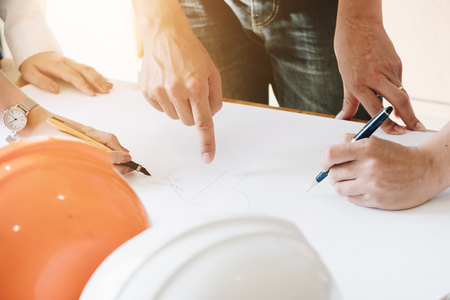 Architect Team Brainstorming Planning Design, Civil engineer sketching a blueprint of construction project with small house model and safety helmet in office, Construction Concept.の写真素材