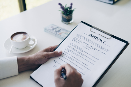 Businessmen holding pen to write business document and contract sheet while sitting at desk with coffee cup and money in home office, Business and Office concept.の写真素材