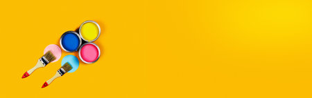Renovation concept. Web banner with yellow background with three color paint cans and two brushes. Flat lay, top view, copy space.の写真素材