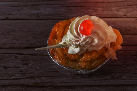puff pastry dough cake with liqueur and cream, a cherry on top and spoon on a wooden tableの写真素材