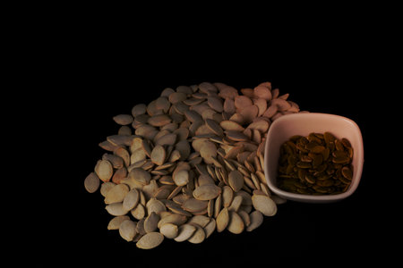 roasted pumpkin seeds roasted with salt in a pile and seeds in a white bowl on a black backgroundの写真素材