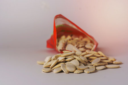 roasted pumpkin seeds with salt coming out of their red bag on a white table with copy space