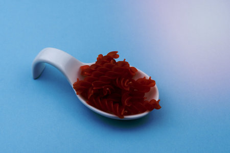 white ceramic spoon with red spiral macaroni and blue backgroundの写真素材
