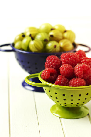 Fresh gooseberries and raspberries in colanders, summer berriesの写真素材