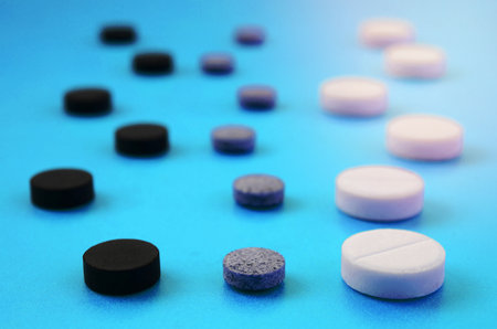 A lot of white, black and grey tablets lie on the blue surface. Background image on medical and...
