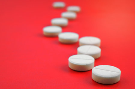 A few white tablets lie on a bright red background surface. Background image on medical and pharmaceutical topicsの写真素材