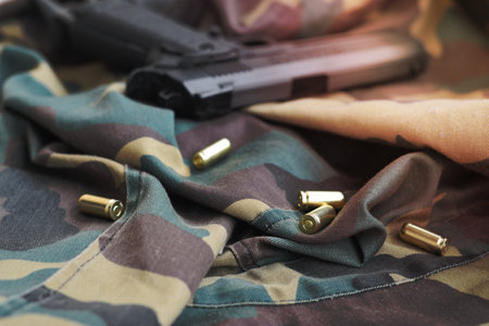 9mm bullets and pistol lie on folded camouflage green fabric. A set shooting range items or a self-defense kit. Golden shells near handgunの写真素材