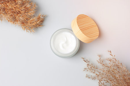 Jar of cosmetic cream with pampas dry grass on white background. Flat lay, copy space