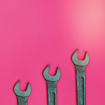 Three metallic spanners lie on texture background of fashion pastel pink color paper in minimal concept.の写真素材