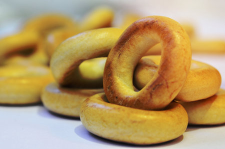 Small heap of golden bagels on white surface. Macro photography