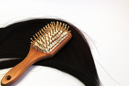 Hair care wooden comb on a long strand of black hair on a white background. Tools from biological materials and natural hair.の写真素材