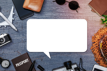 Blank speech bubbles with Traveler's accessories with passport, books of travel plan, wallet, camera, hat, backpack and airplane toy on blue wooden desk, Flat lay with copy space, Travel concept backgroundの写真素材