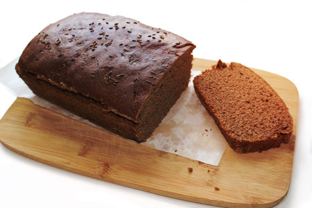 Sliced dark rye hemp seed bread on paper and wooden board on white background