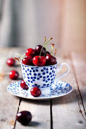 Fresh cherry in a blue ceramic cup on a wooden backgroundの写真素材