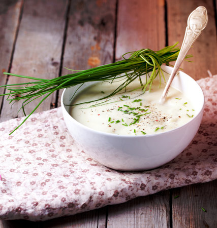 Cauliflower, parsnip, potato, celery soup with chives in a white ceramic bowl on a wooden backgroundの写真素材