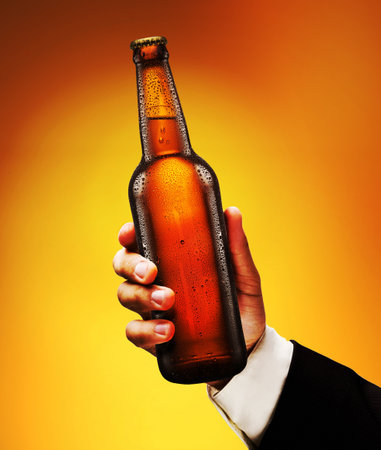 Bottle of beer in a man's hand on a yellow background.の写真素材