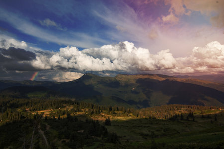 Fluffy clouds above valley landscape photo. Beautiful nature scenery photography with rainbow on background. Ambient light. High quality picture for wallpaper, travel blog, magazine, articleの写真素材