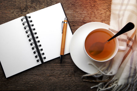 Open notebook and cup of tea on wooden backgroundの写真素材
