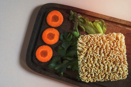 Yellow instant noodle has vegetable ingredient on pink wood background, top view, Asian food concept.の写真素材