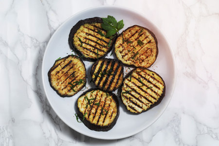 Grilled eggplants in plate isolated on white marble background close up, top view, healthy food concept.の写真素材