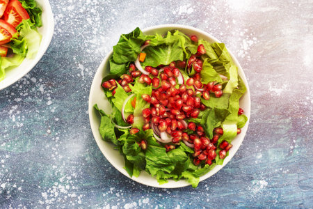 Pomegranate salad has romaine lettuce in bowl isolated on blue wood background close up, top view, healthy vegetable food concept.の写真素材