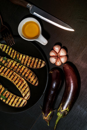 Grilled eggplants in black plate has fork and olive oil garlic on isolated on wood background close up, top view, healthy food concept.の写真素材