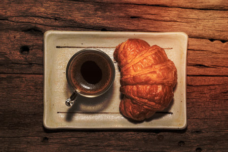 Espresso coffee and croissant in plate on isolated wood table background close up, top view, breakfast food and drink concept.の写真素材